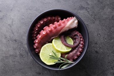 Fresh raw octopus, lemon and rosemary in bowl on grey table, top view