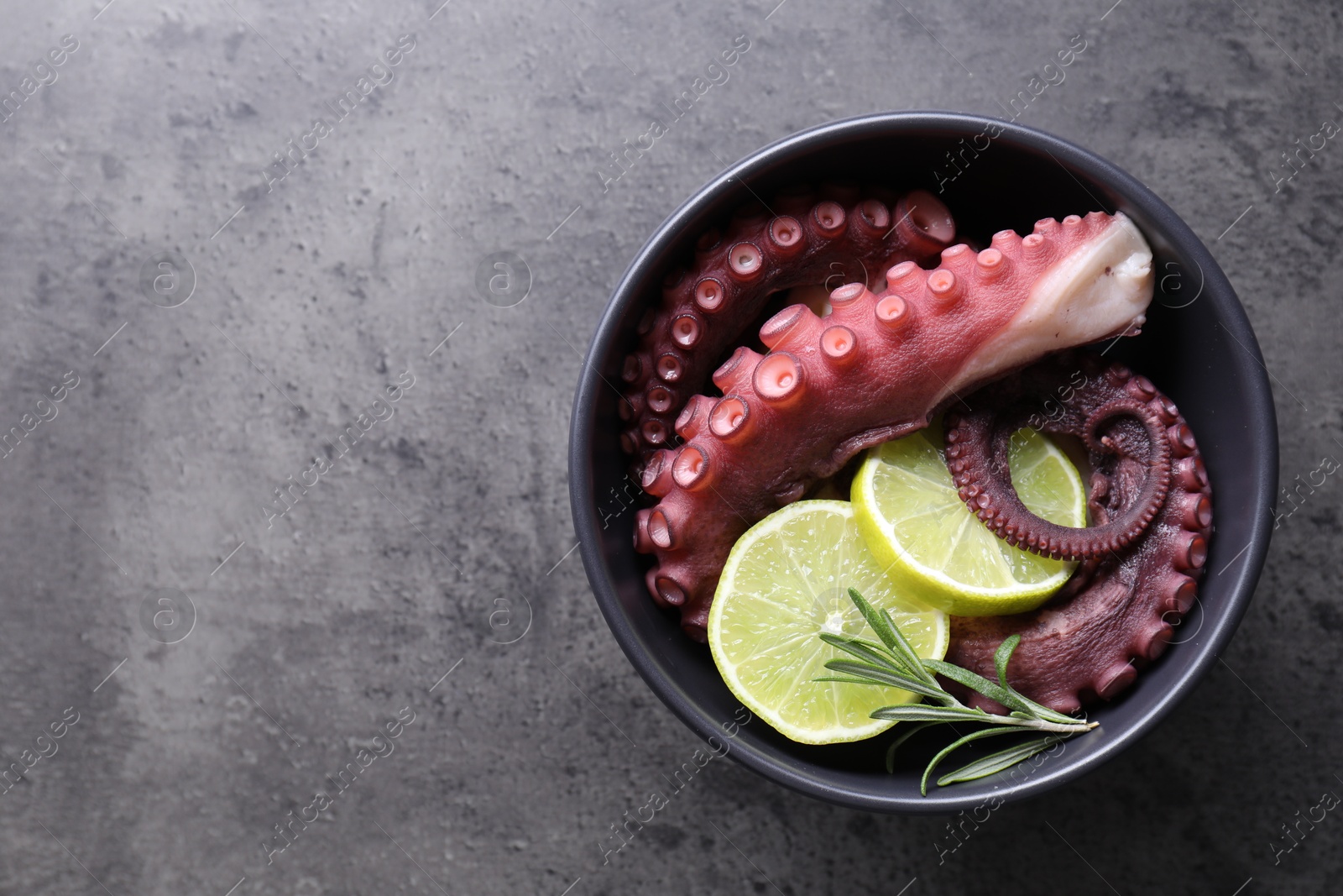 Photo of Fresh raw octopus, lemon and rosemary in bowl on grey table, top view. Space for text