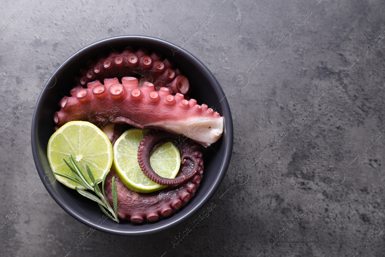 Photo of Fresh raw octopus, lemon and rosemary in bowl on grey table, top view. Space for text