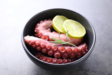 Fresh raw octopus, lemon and rosemary in bowl on grey table, closeup