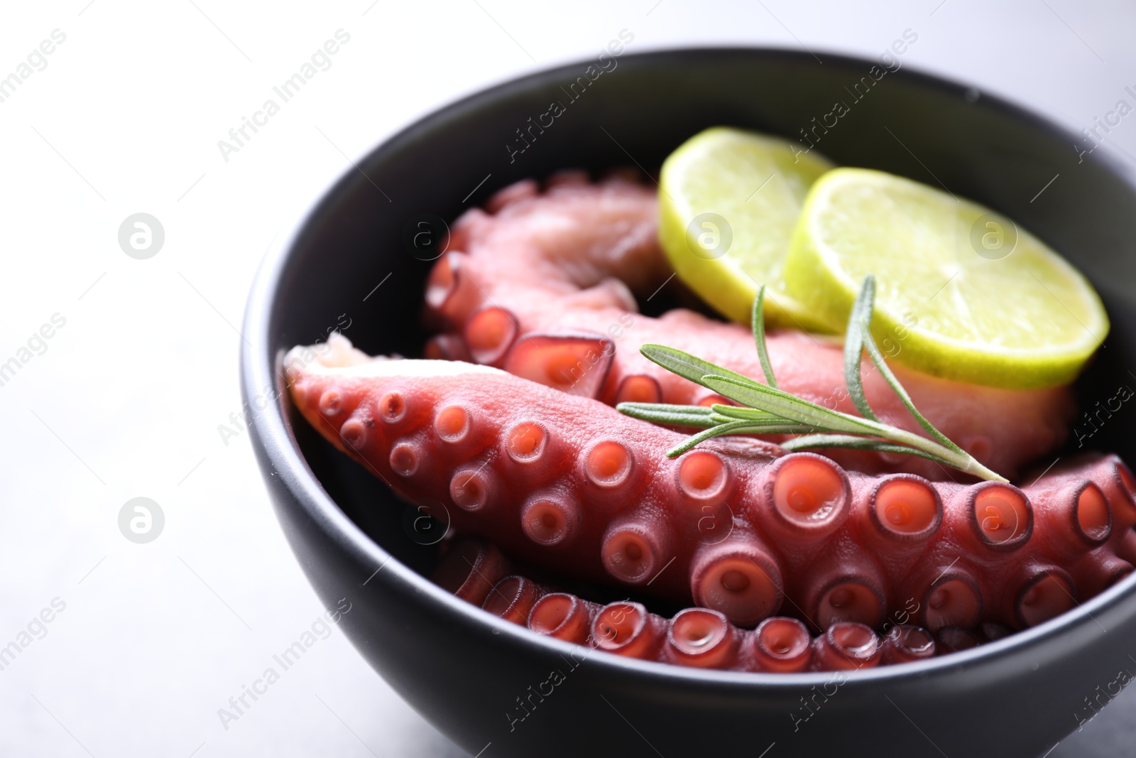 Photo of Fresh raw octopus, lemon and rosemary in bowl on grey table, closeup