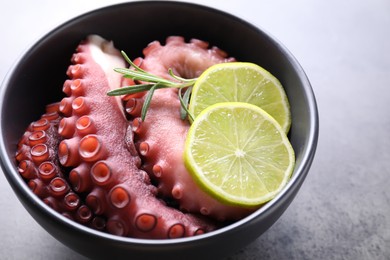 Photo of Fresh raw octopus, lemon and rosemary in bowl on grey table, closeup