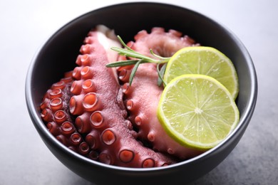 Photo of Fresh raw octopus, lemon and rosemary in bowl on grey table, closeup