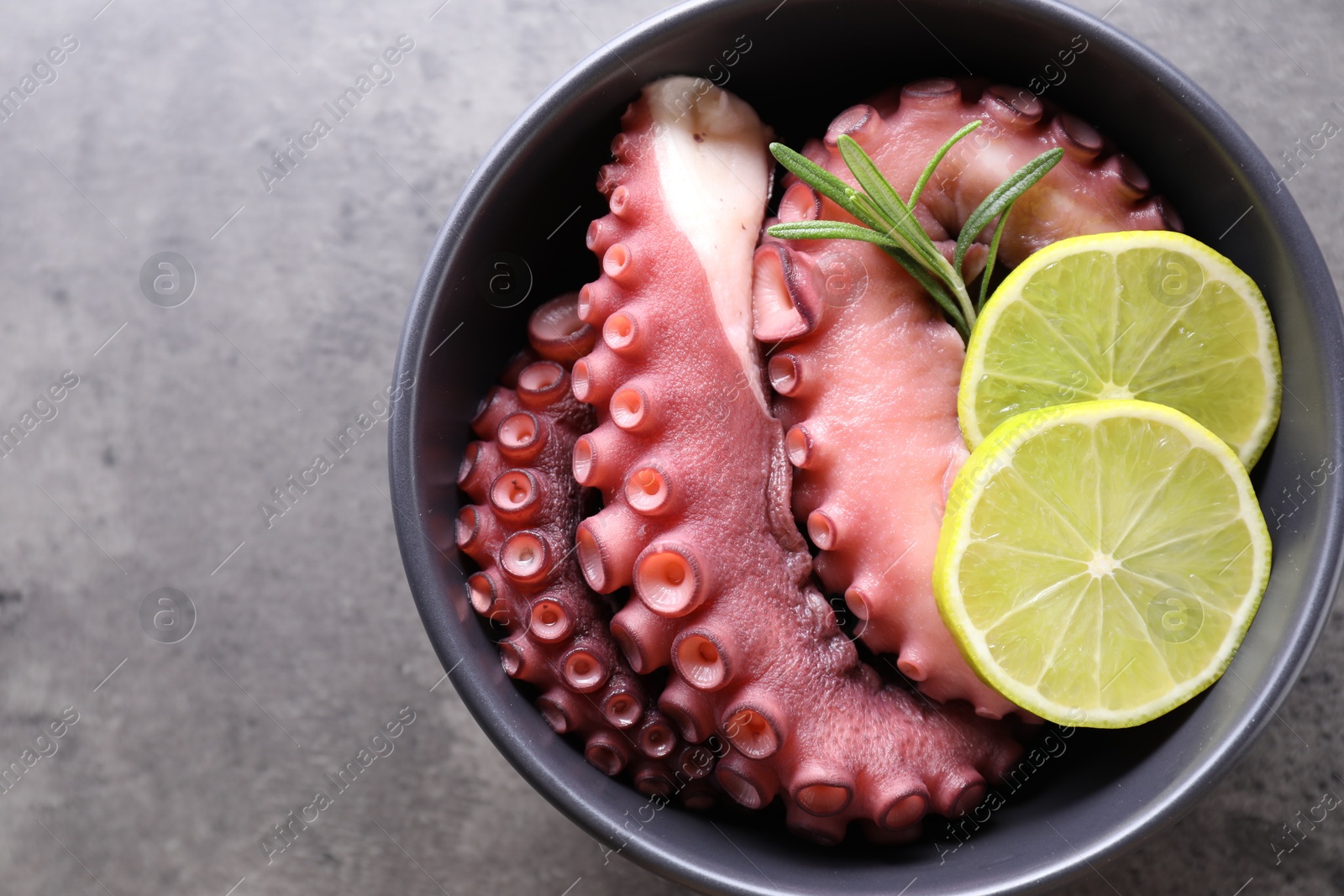 Photo of Fresh raw octopus, lemon and rosemary in bowl on grey table, top view