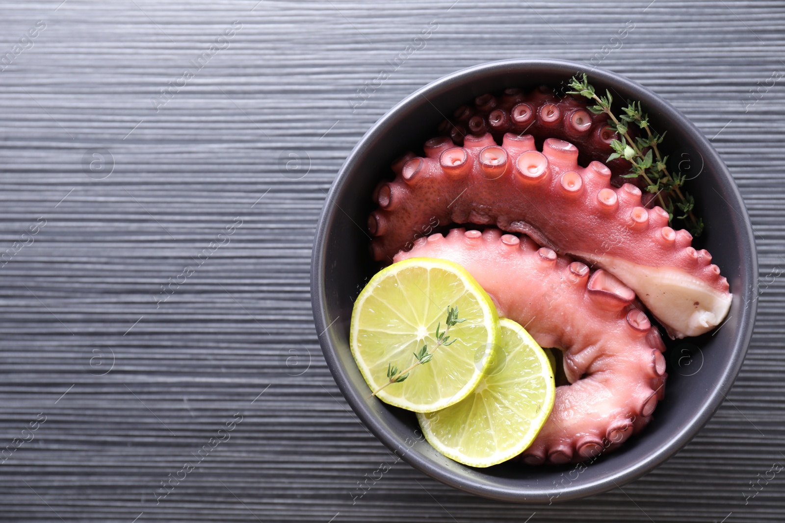 Photo of Fresh raw octopus, lemon and thyme in bowl on dark textured table, top view. Space for text