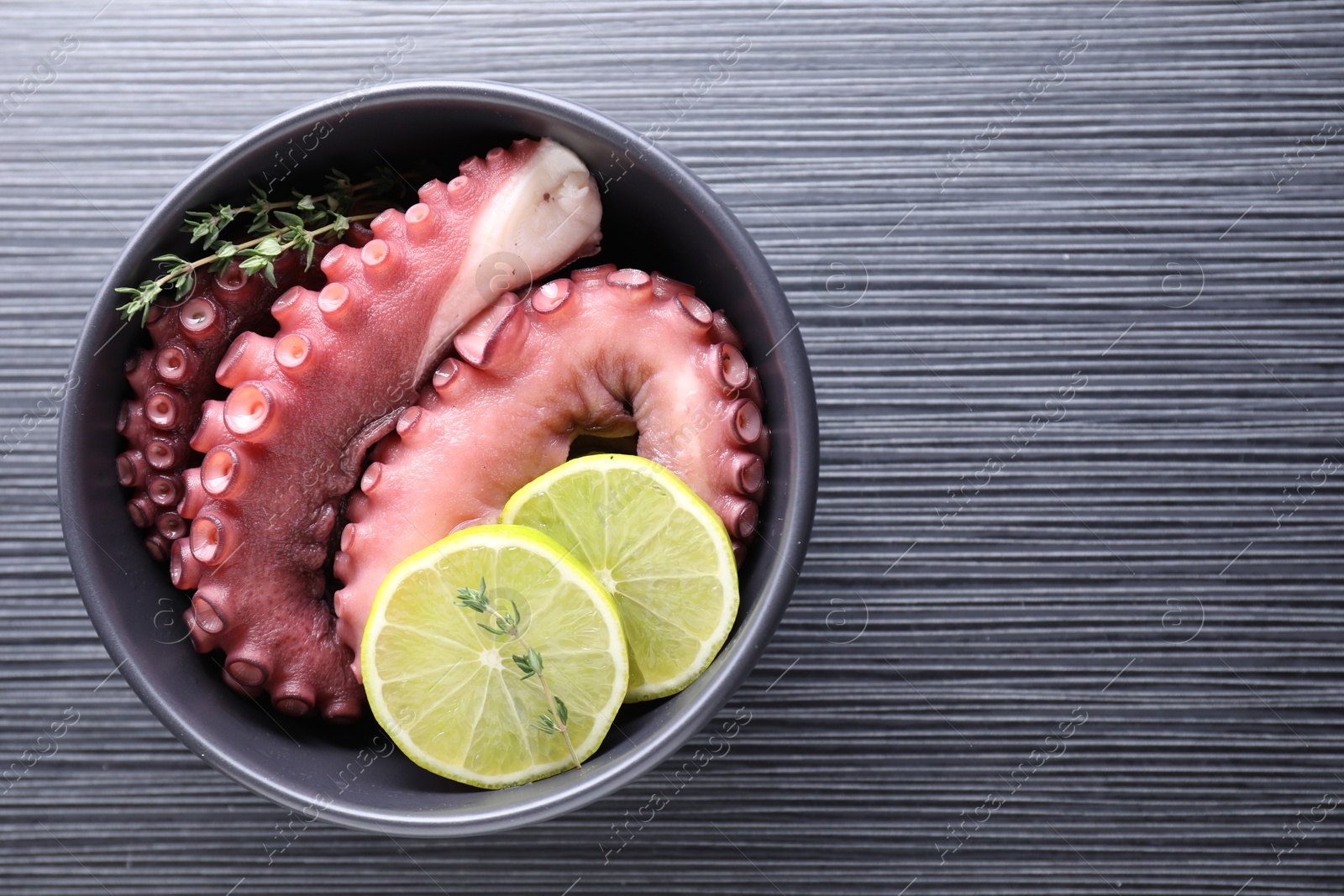 Photo of Fresh raw octopus, lemon and thyme in bowl on dark textured table, top view. Space for text