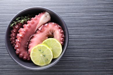 Photo of Fresh raw octopus, lemon and thyme in bowl on dark textured table, top view. Space for text