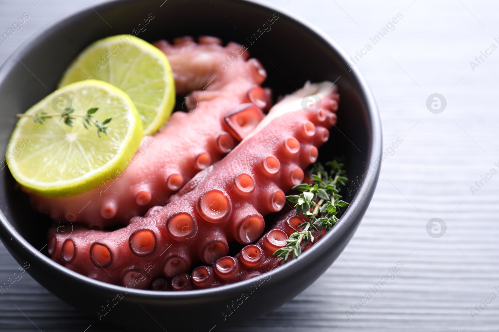 Photo of Fresh raw octopus, lemon and thyme in bowl on table, closeup