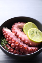 Photo of Fresh raw octopus, lemon and thyme in bowl on table, closeup