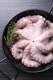 Fresh raw octopus and thyme in frying pan on dark textured table, top view