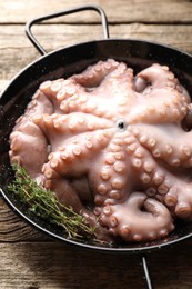 Photo of Fresh raw octopus and thyme in frying pan on wooden table, closeup