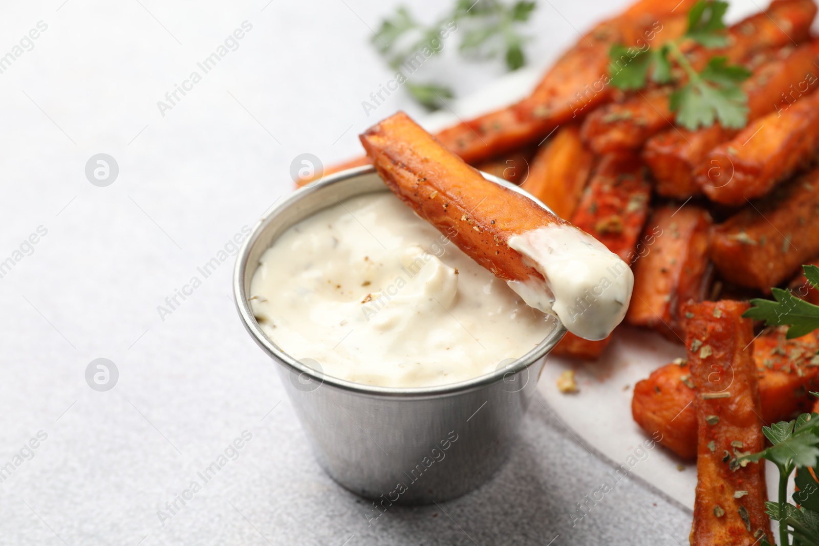 Photo of Delicious sweet potato fries with spices and sauce on light grey table, closeup