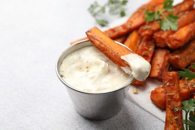 Photo of Delicious sweet potato fries with spices and sauce on light grey table, closeup