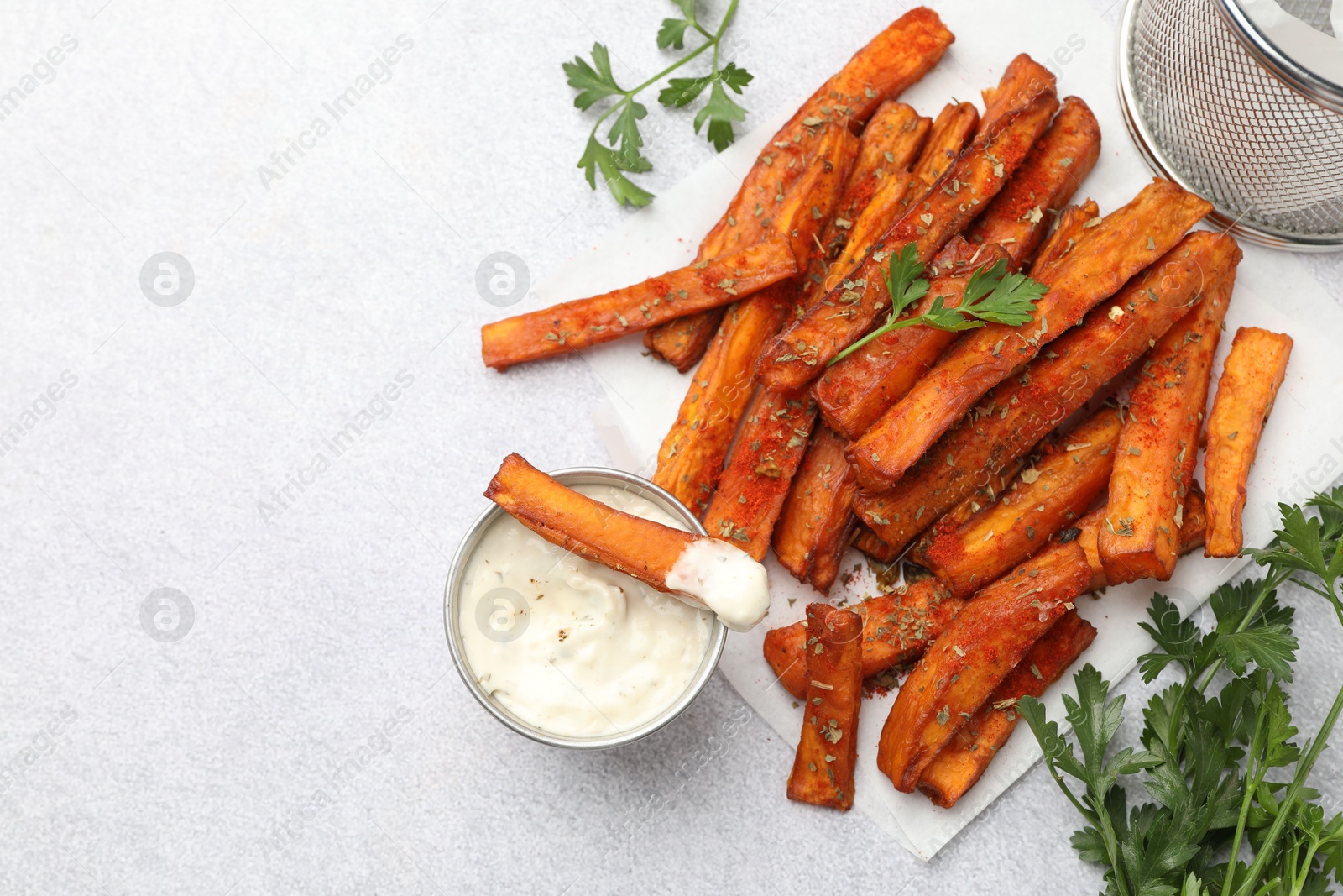 Photo of Delicious sweet potato fries with spices and sauce on light grey table, top view. Space for text