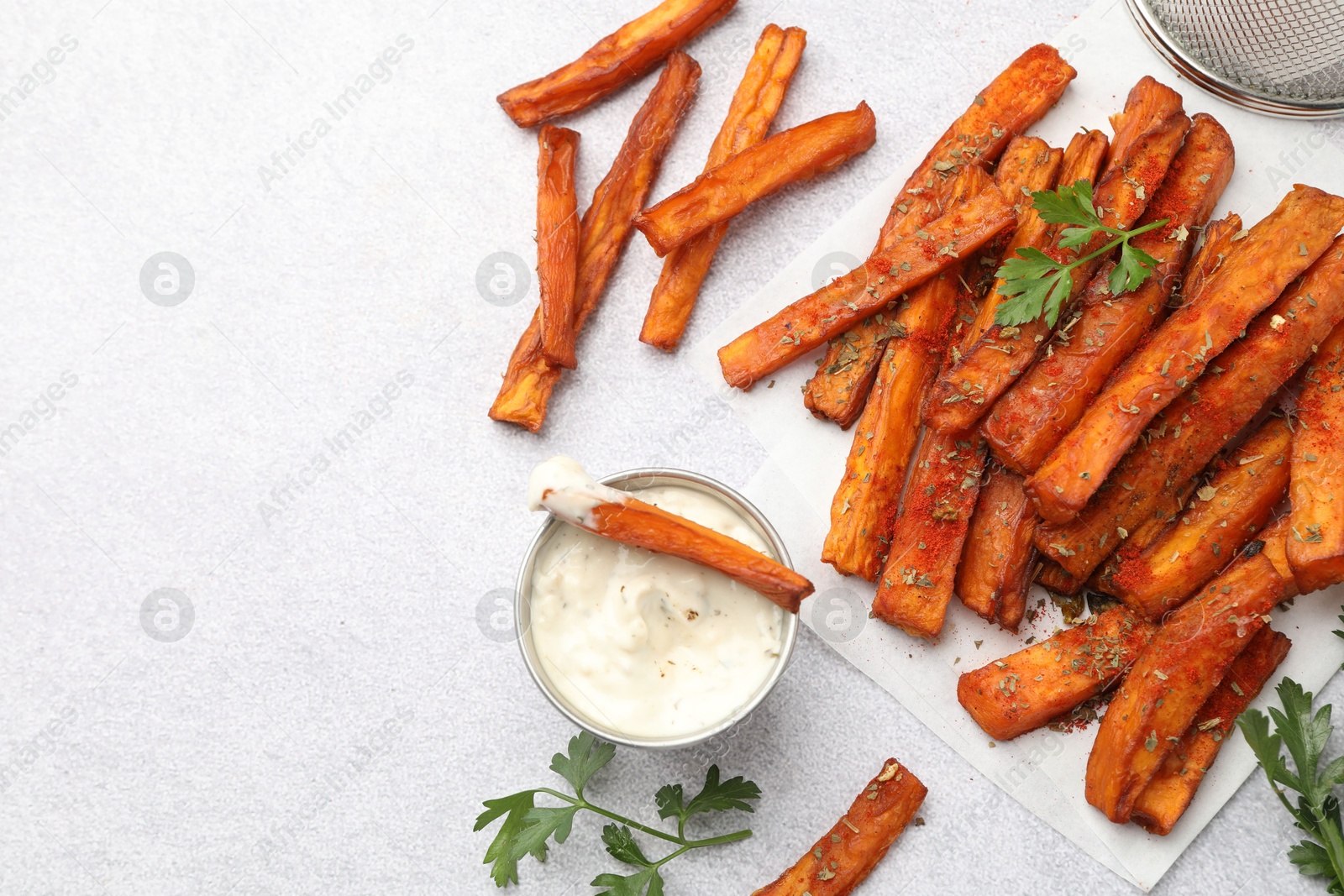 Photo of Delicious sweet potato fries with spices and sauce on light grey table, top view. Space for text