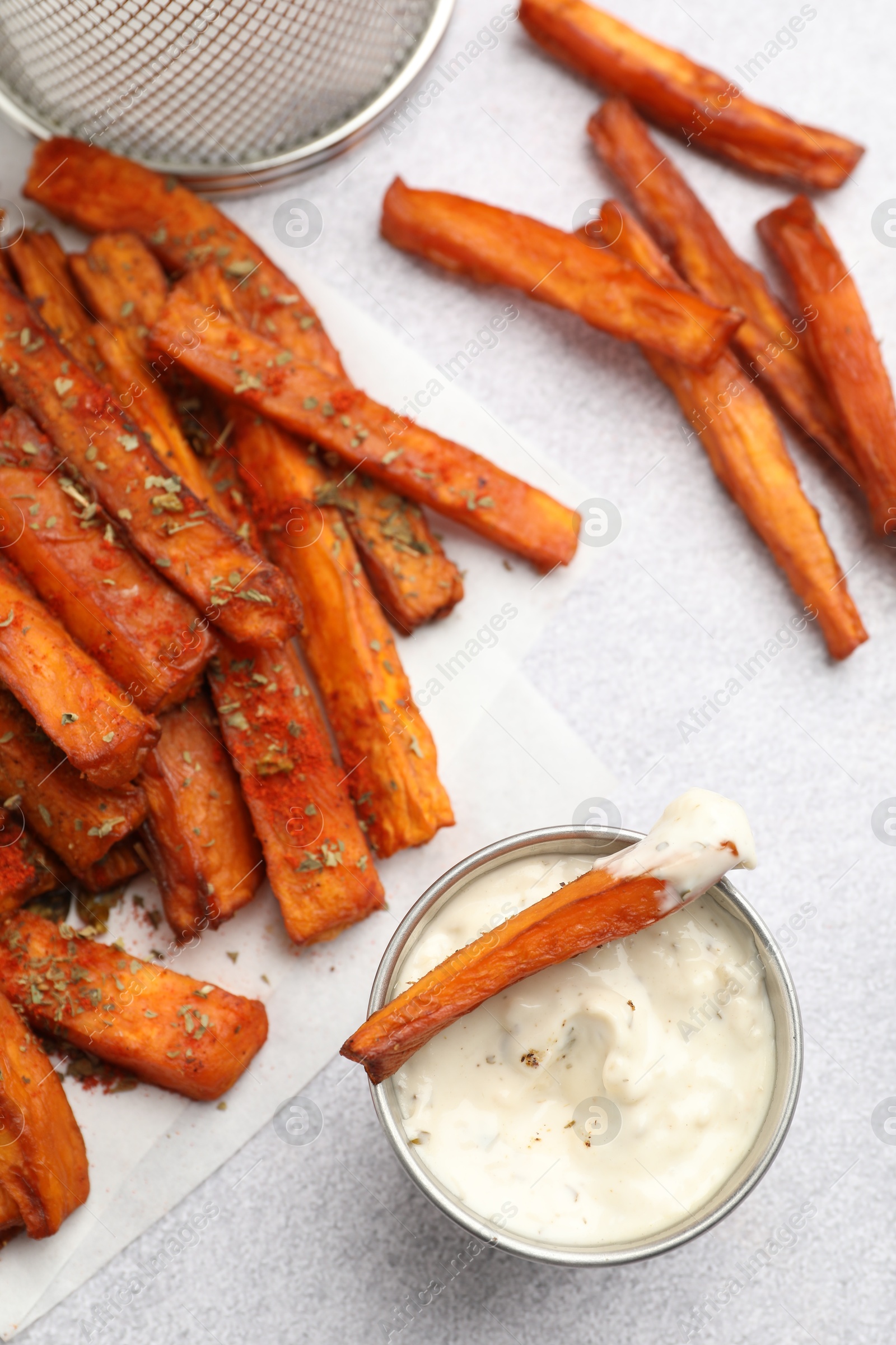 Photo of Delicious sweet potato fries with spices and sauce on light grey table, top view