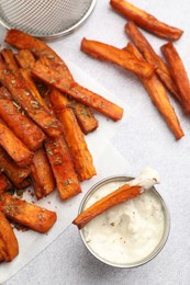 Photo of Delicious sweet potato fries with spices and sauce on light grey table, top view