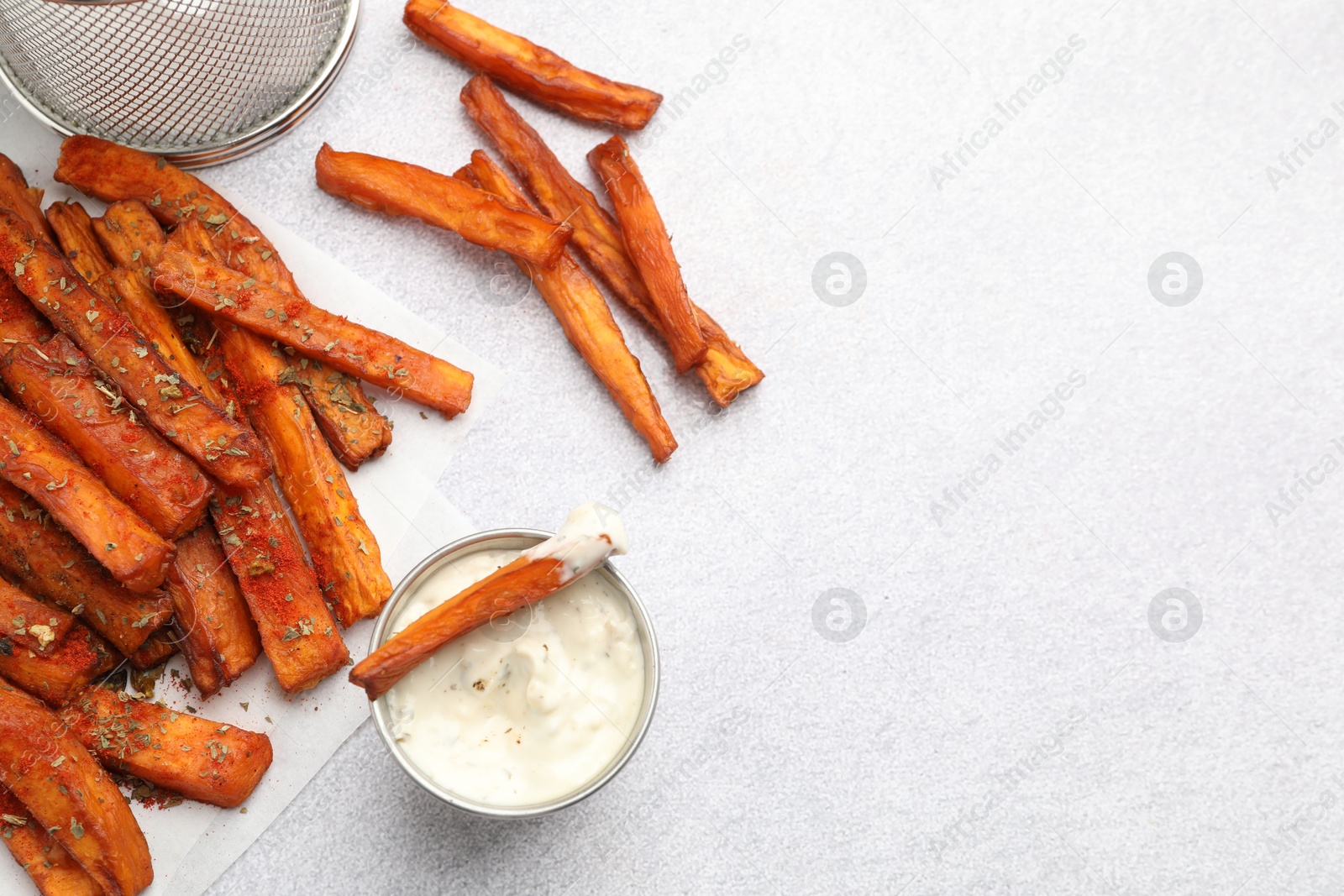 Photo of Delicious sweet potato fries with spices and sauce on light grey table, top view. Space for text