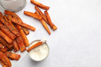 Delicious sweet potato fries with spices and sauce on light grey table, top view. Space for text