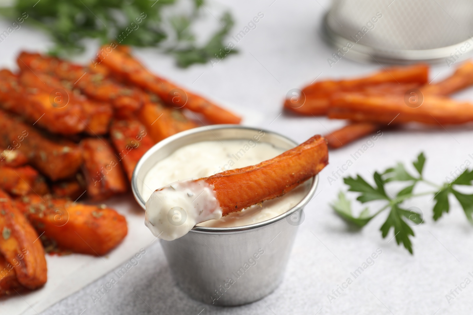 Photo of Delicious sweet potato fries, sauce and parsley on light grey table, closeup