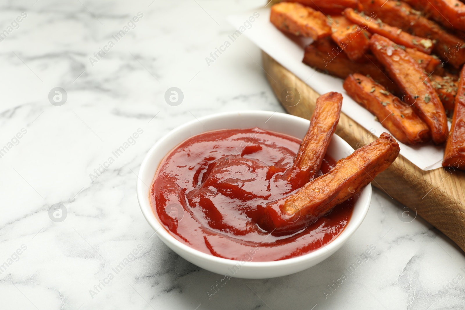 Photo of Delicious sweet potato fries with spices and sauce on white marble table, closeup