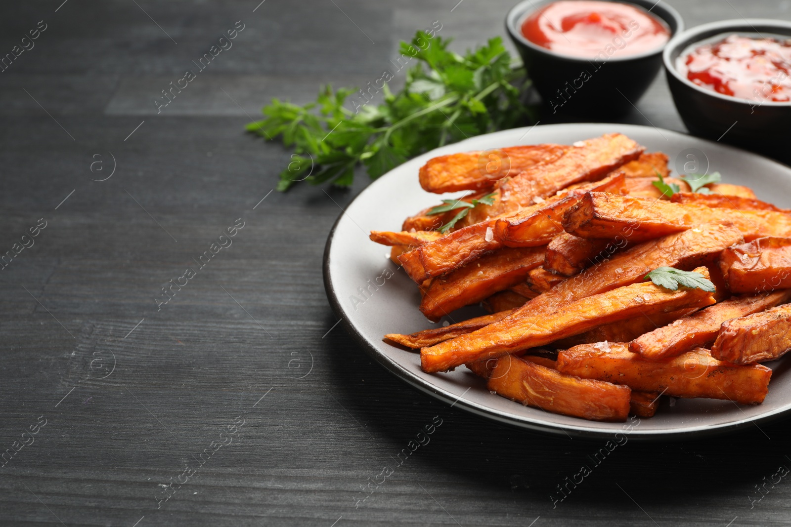 Photo of Delicious sweet potato fries with spices and sauces on black wooden table, closeup. Space for text