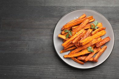 Photo of Delicious sweet potato fries with spices on black wooden table, top view. Space for text