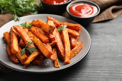 Photo of Delicious sweet potato fries with spices and sauces on black wooden table, closeup