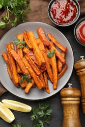 Photo of Delicious sweet potato fries with spices and sauces on black wooden table, top view