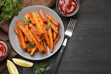 Delicious sweet potato fries with spices and sauces on black wooden table, top view. Space for text