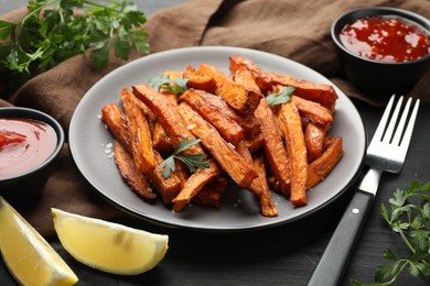 Photo of Delicious sweet potato fries with spices and sauces on black wooden table, closeup