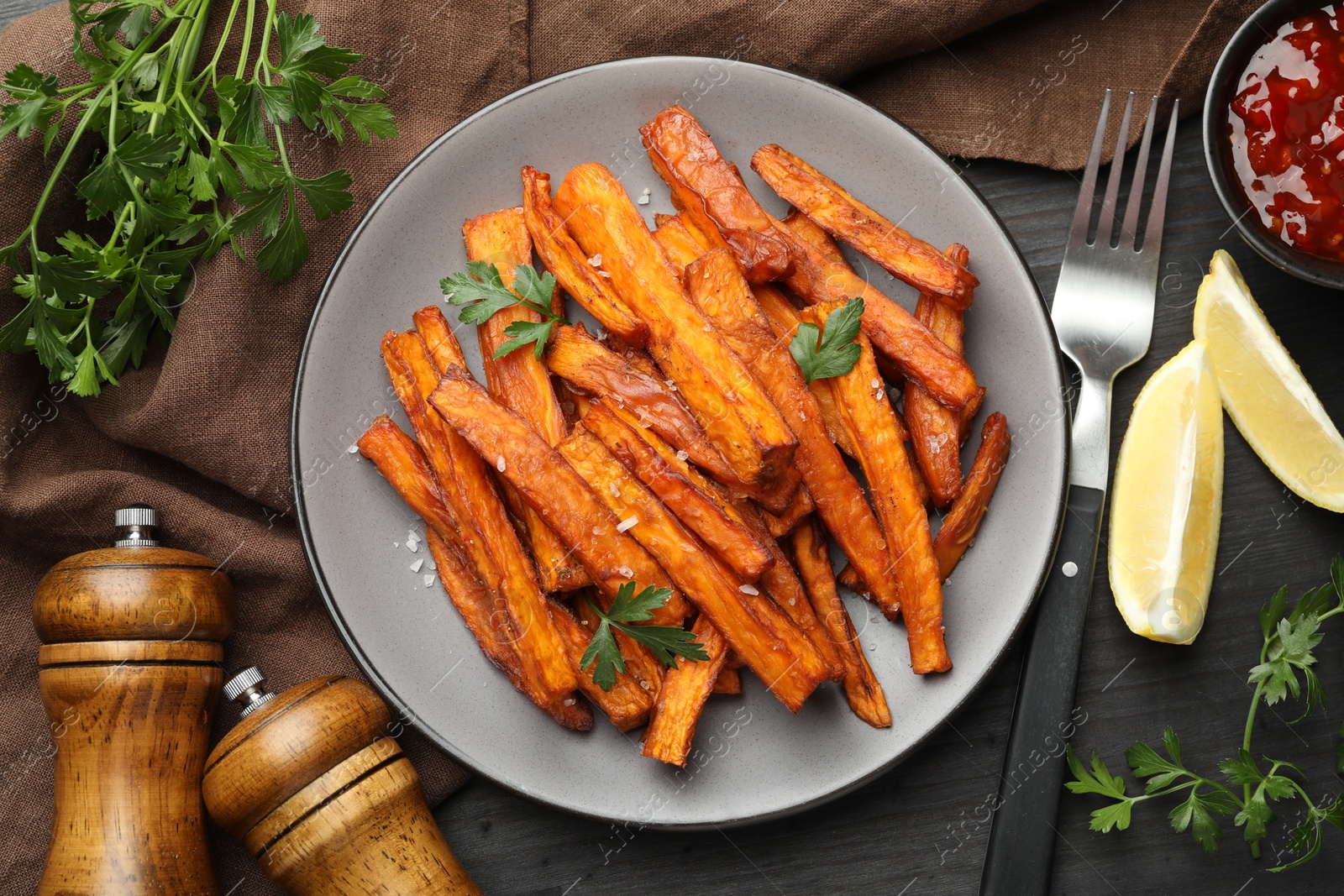 Photo of Delicious sweet potato fries with spices and sauce on black wooden table, top view