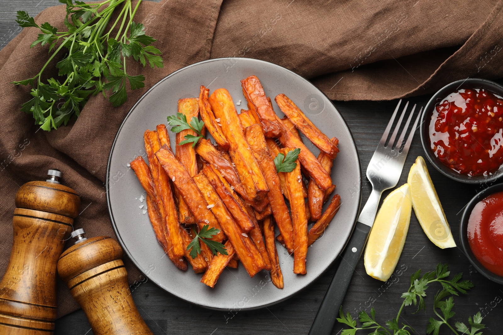 Photo of Delicious sweet potato fries with spices and sauces on black wooden table, top view