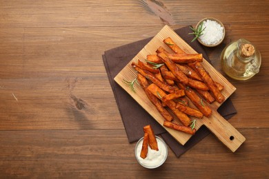 Photo of Delicious sweet potato fries with spices, sauce and oil on wooden table, top view. Space for text