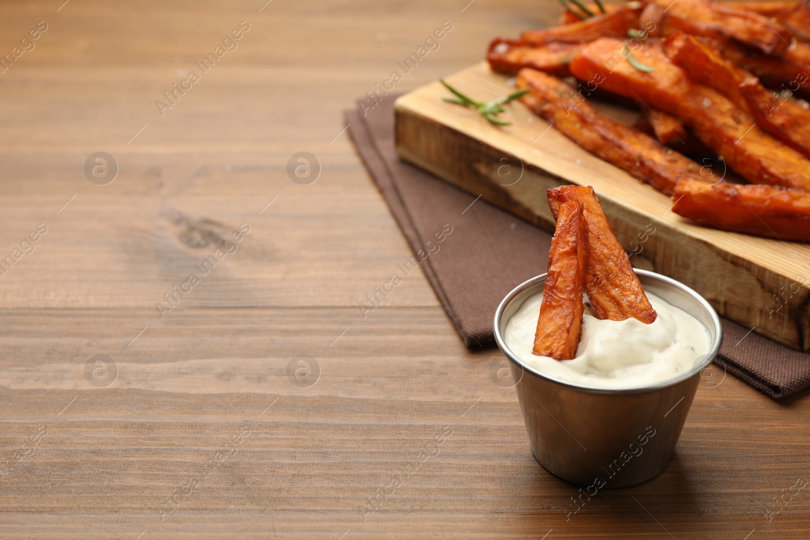 Photo of Delicious sweet potato fries and sauce on wooden table. Space for text