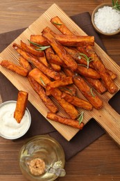 Photo of Delicious sweet potato fries with spices, sauce and oil on wooden table, top view