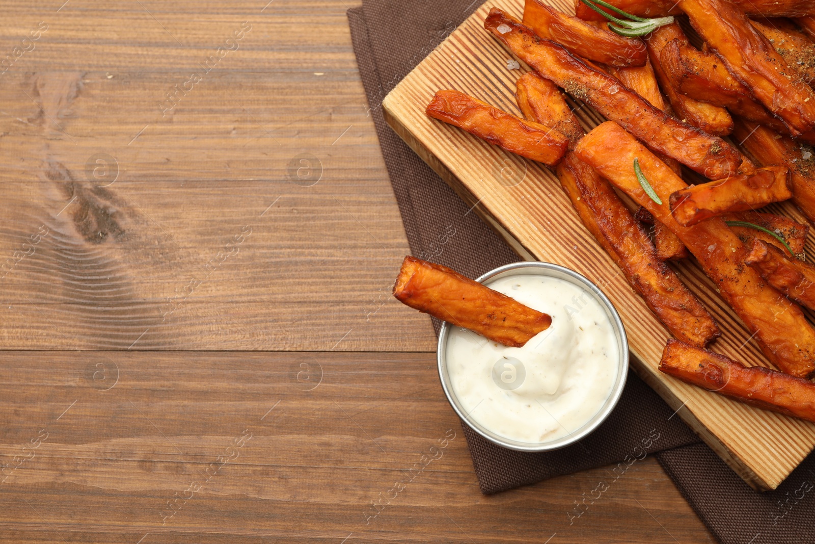 Photo of Delicious sweet potato fries with spices and sauce on wooden table, top view. Space for text