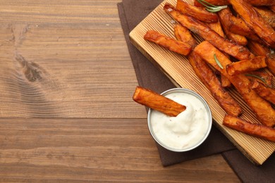 Delicious sweet potato fries with spices and sauce on wooden table, top view. Space for text