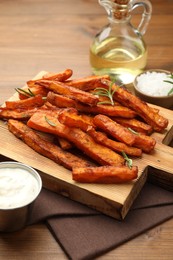 Delicious sweet potato fries with spices, sauce and oil on wooden table, closeup