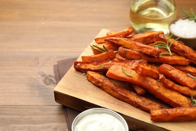 Photo of Delicious sweet potato fries with spices and sauce on wooden table, closeup. Space for text