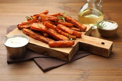 Photo of Delicious sweet potato fries with spices, sauce and oil on wooden table