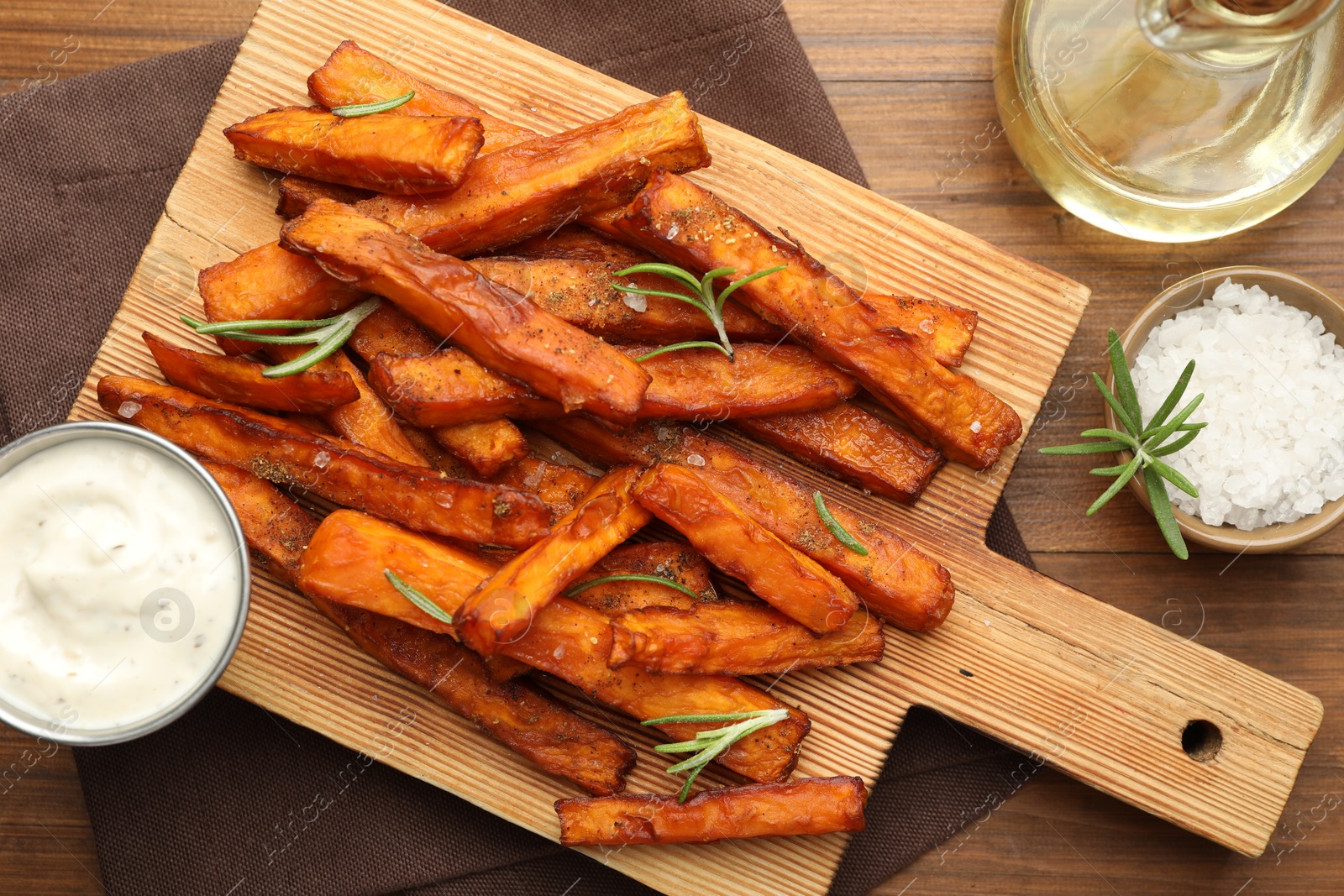 Photo of Delicious sweet potato fries with spices, sauce and oil on wooden table, top view