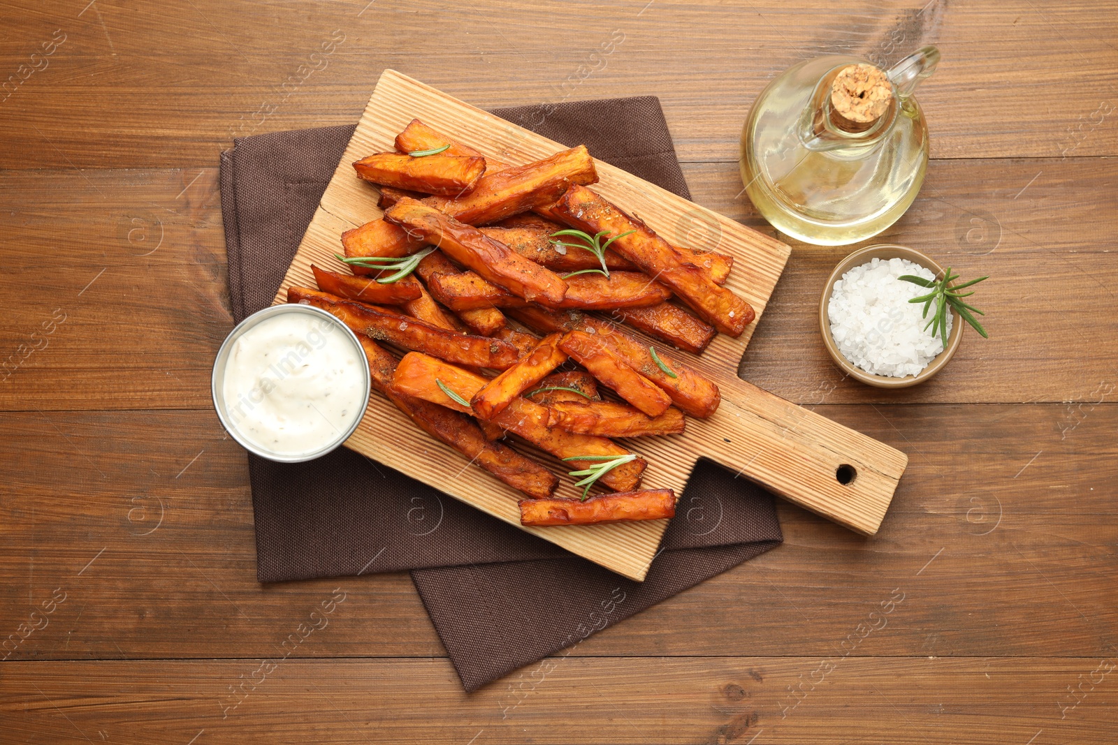 Photo of Delicious sweet potato fries with spices, sauce and oil on wooden table, top view