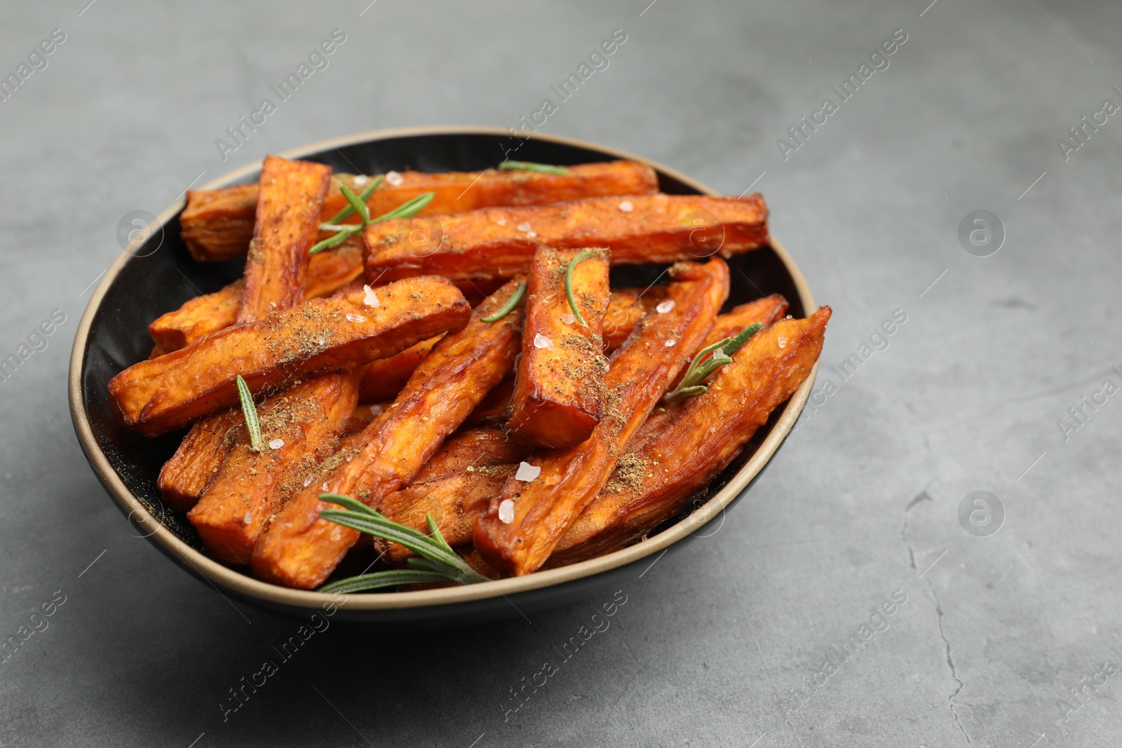 Photo of Delicious sweet potato fries with spices in bowl on grey table, closeup