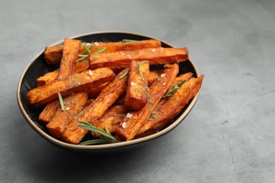 Photo of Delicious sweet potato fries with spices in bowl on grey table, closeup