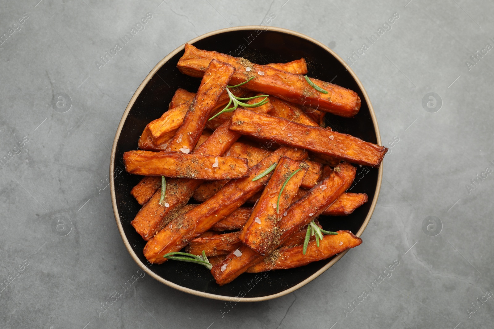 Photo of Delicious sweet potato fries with spices in bowl on grey table, top view