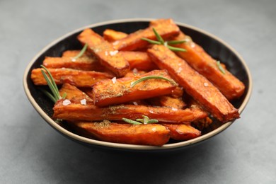 Photo of Delicious sweet potato fries with spices in bowl on grey table, closeup