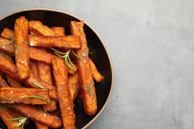 Photo of Delicious sweet potato fries with spices in bowl on grey table, top view. Space for text