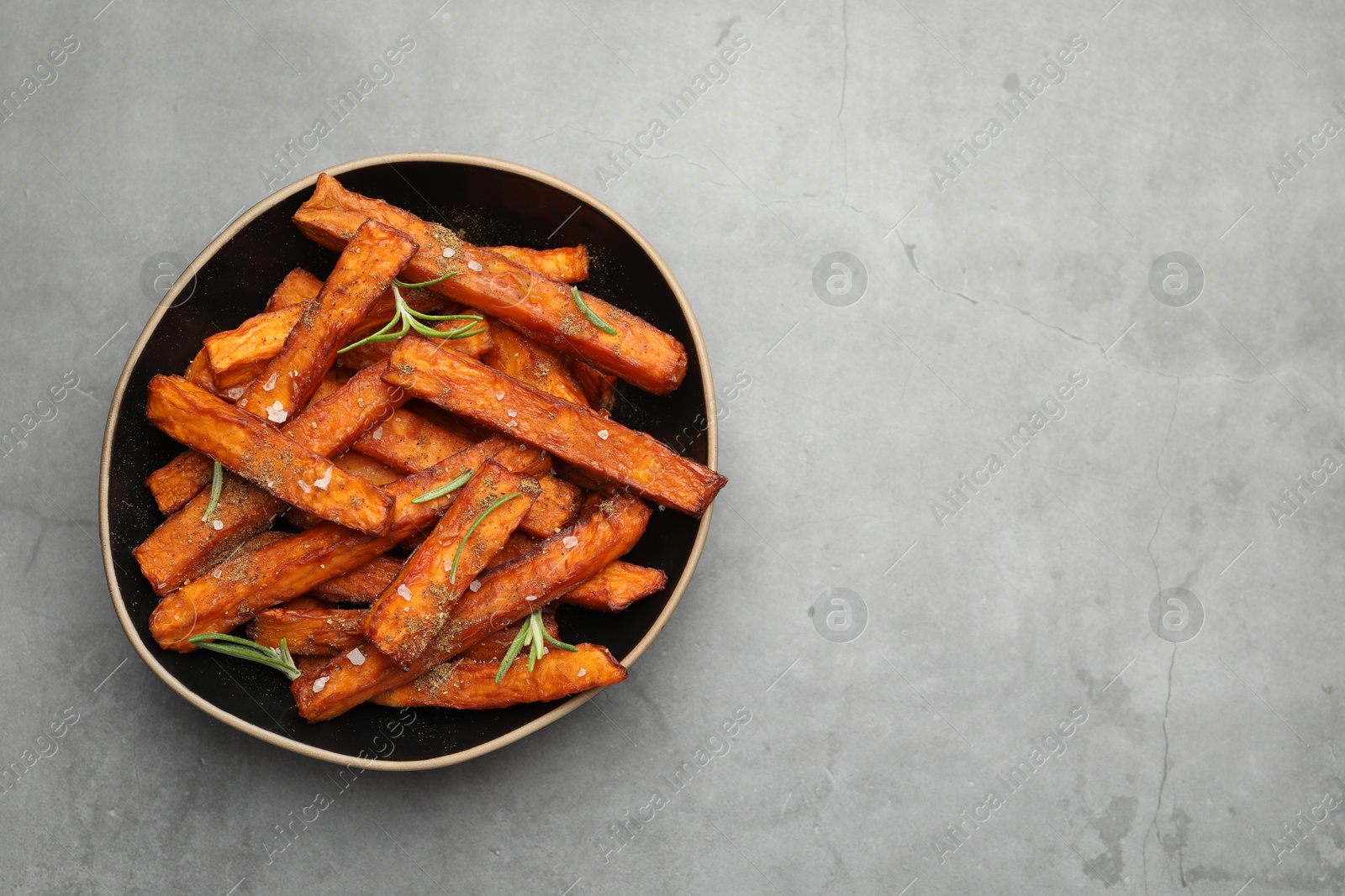 Photo of Delicious sweet potato fries with spices in bowl on grey table, top view. Space for text