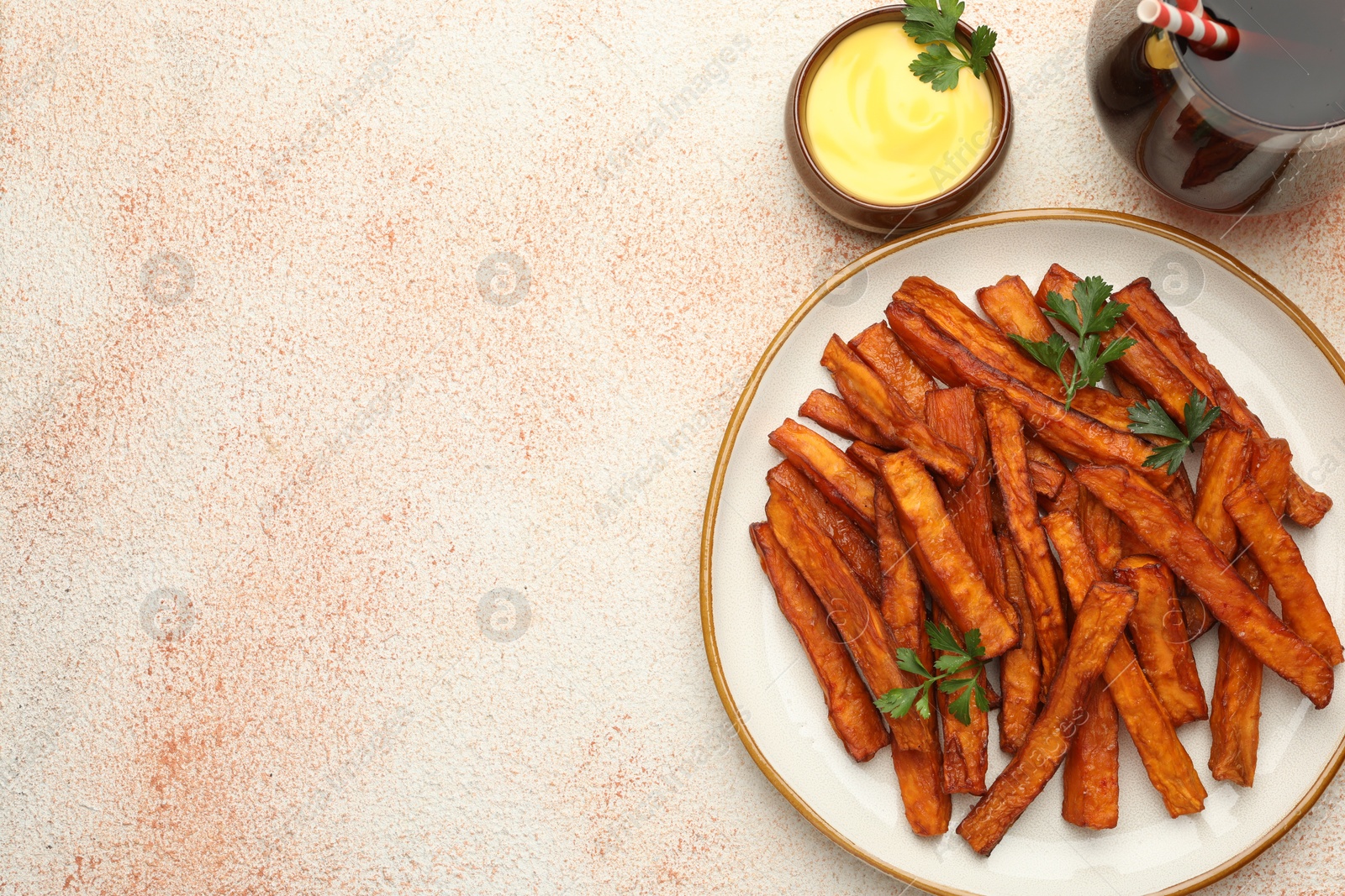 Photo of Delicious sweet potato fries, parsley, sauce and soda drink on beige textured table, top view. Space for text